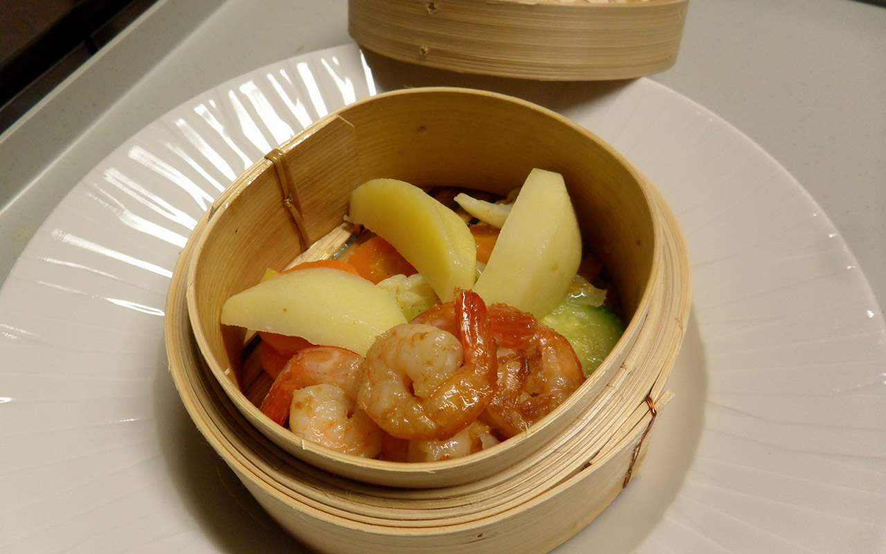 Gamberi, patate e verdure cotte in un recipiente di bamboo